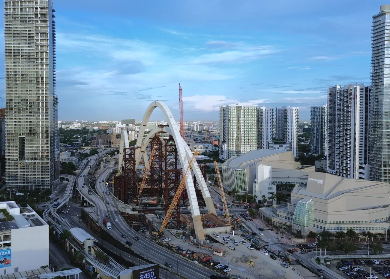 September 2026: the I-395 Signature Bridge in Miami with its white arches standing over the highway, seen from a drone above Museum Park.
