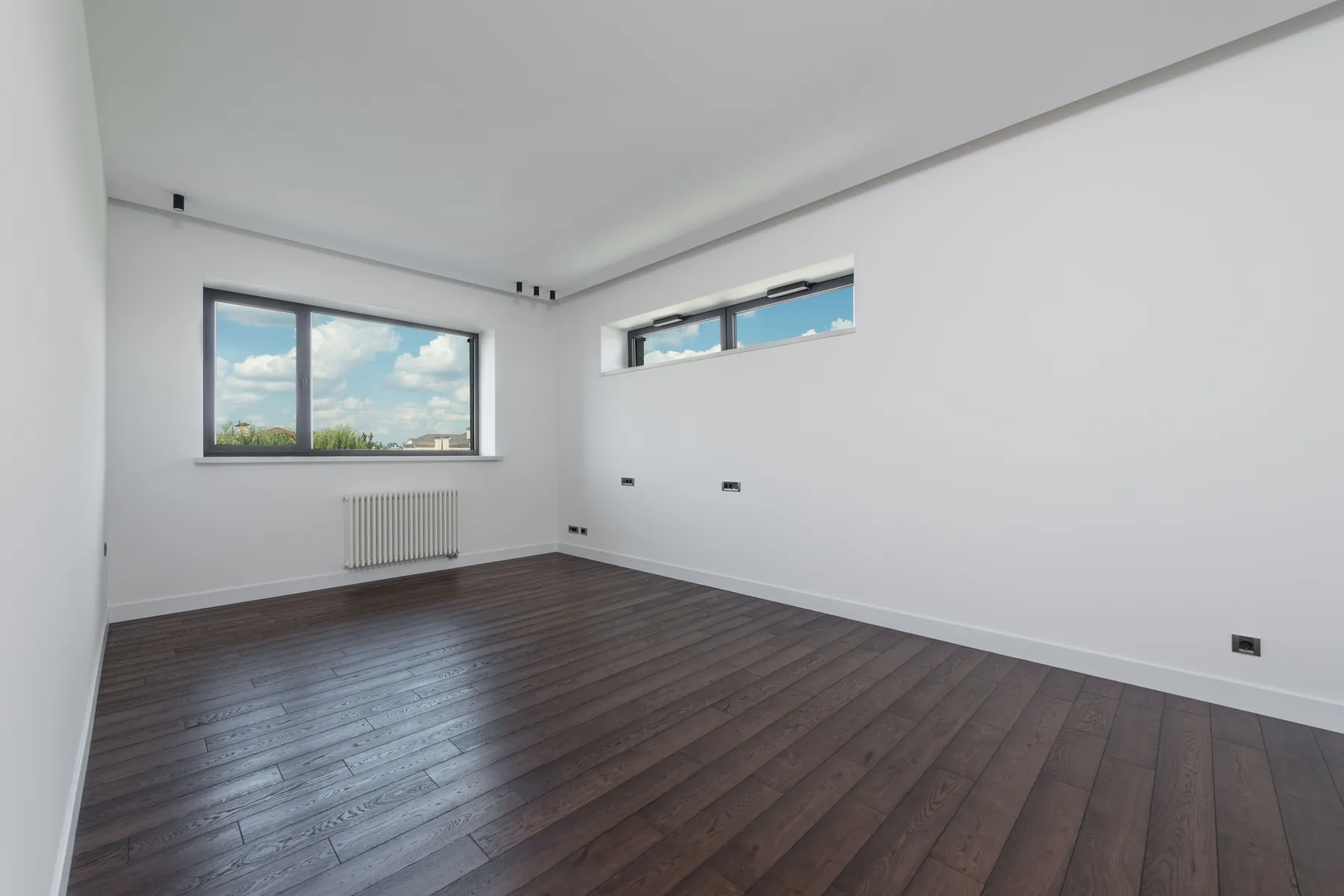 Before: an empty living room with white walls, dark wood flooring, a wide window and a high strip window.